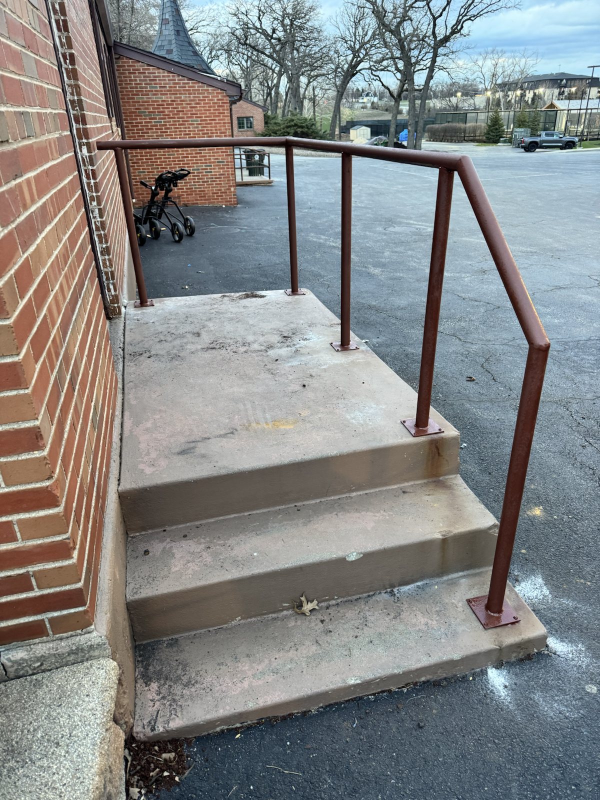 Older brown exterior handrail on concrete steps before repaint or replacement.