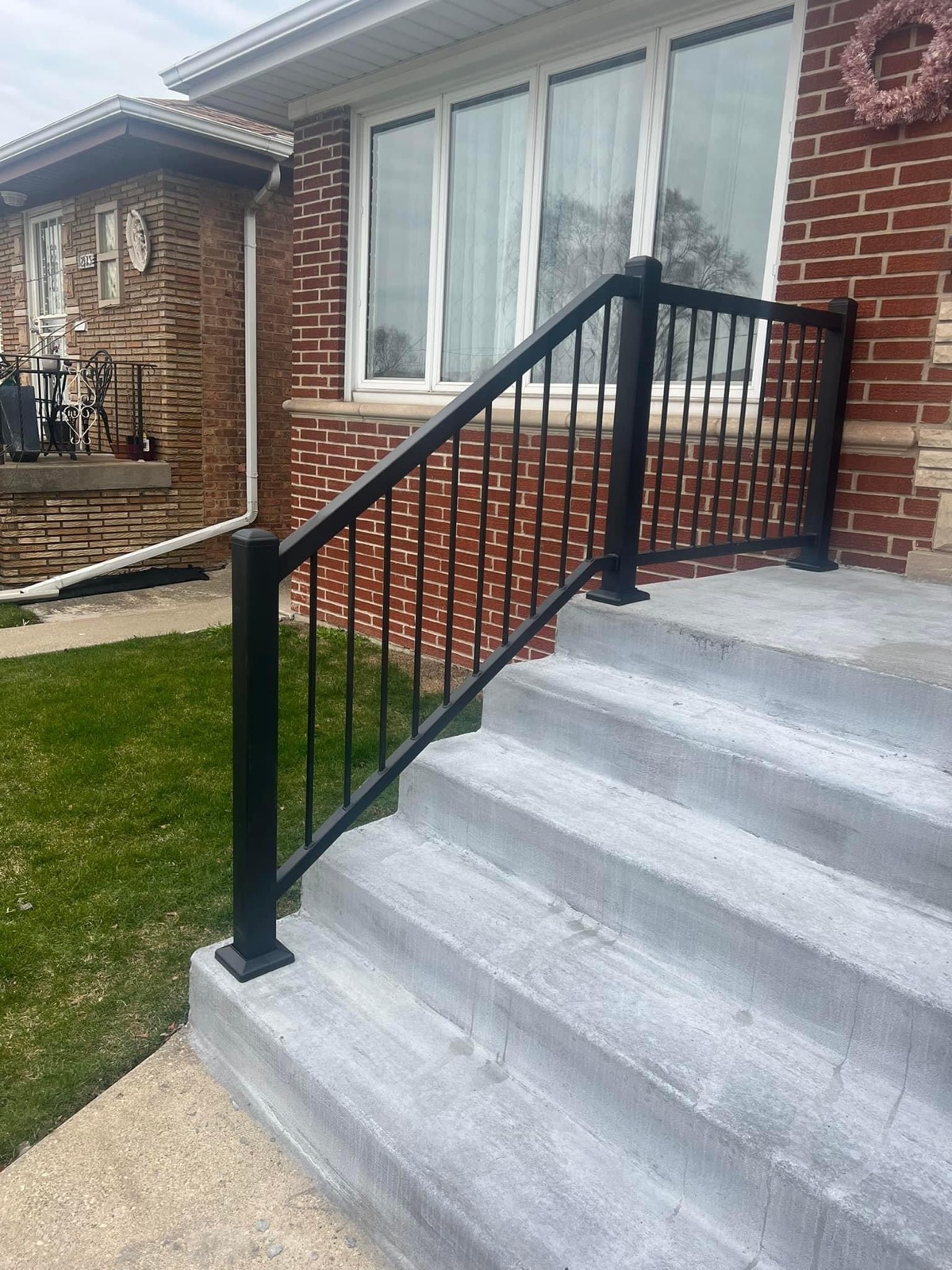 Modern black steel railing installed on newly refinished concrete front steps.
