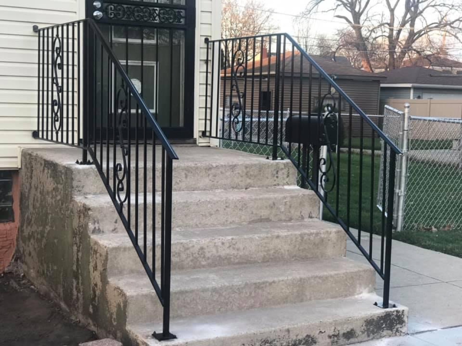 Black steel front step railings with decorative scroll details installed on a residential entry.