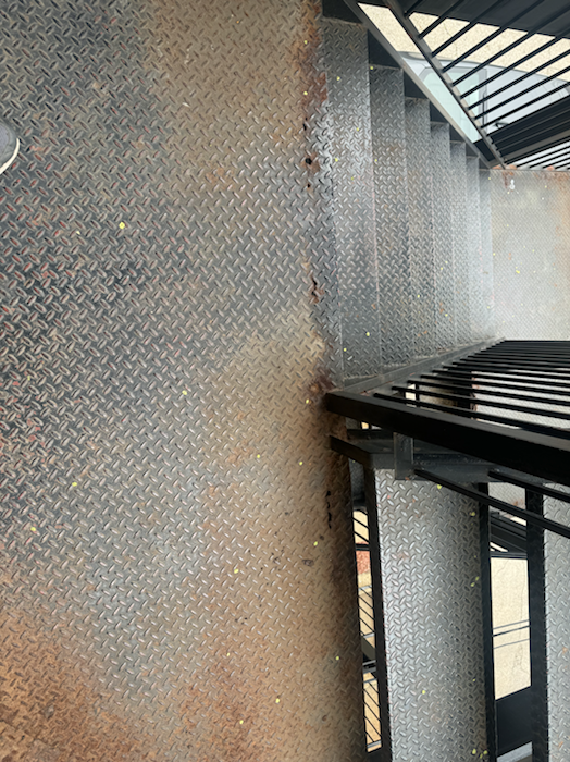 Metal porch deck and stair surface with rust damage and worn steel before restoration.