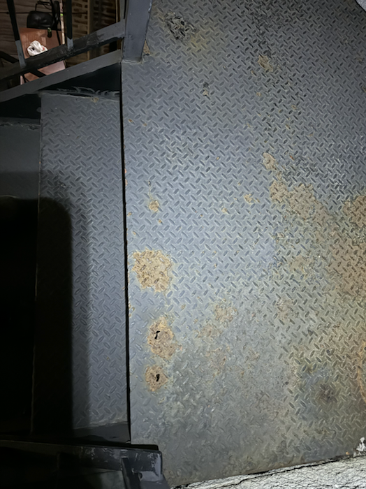 Steel landing surface with failing paint and worn coating before restoration work.