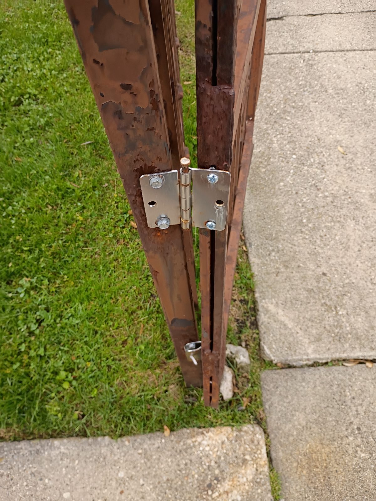 Close-up of a rusted pedestrian gate hinge area before repair.