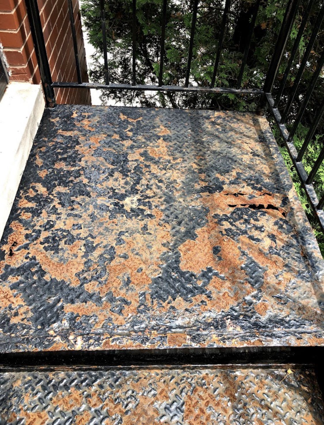 Severely rusted exterior metal landing with holes before front-entry repair.