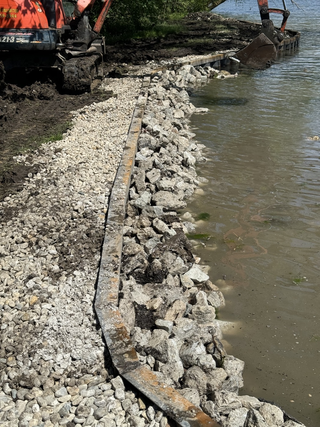 Rip rap shoreline installation at the water edge with equipment working near the lake.